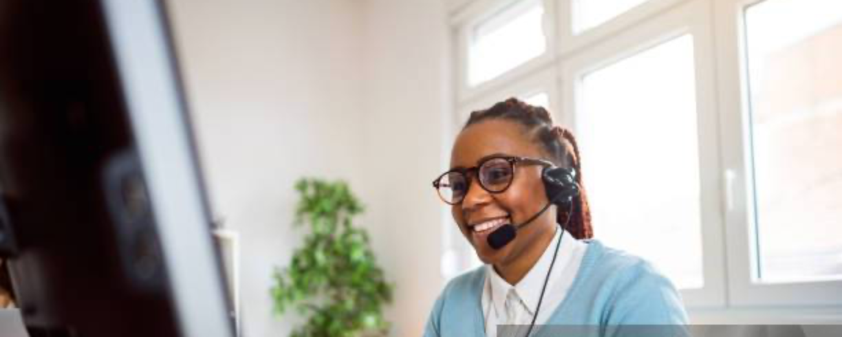 A school front-office staff member wearing a headset, smiling while answering calls at her desk